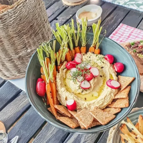 Antipastifat med hummus, nypegulrøtter og sukkererter servert på tallerken.